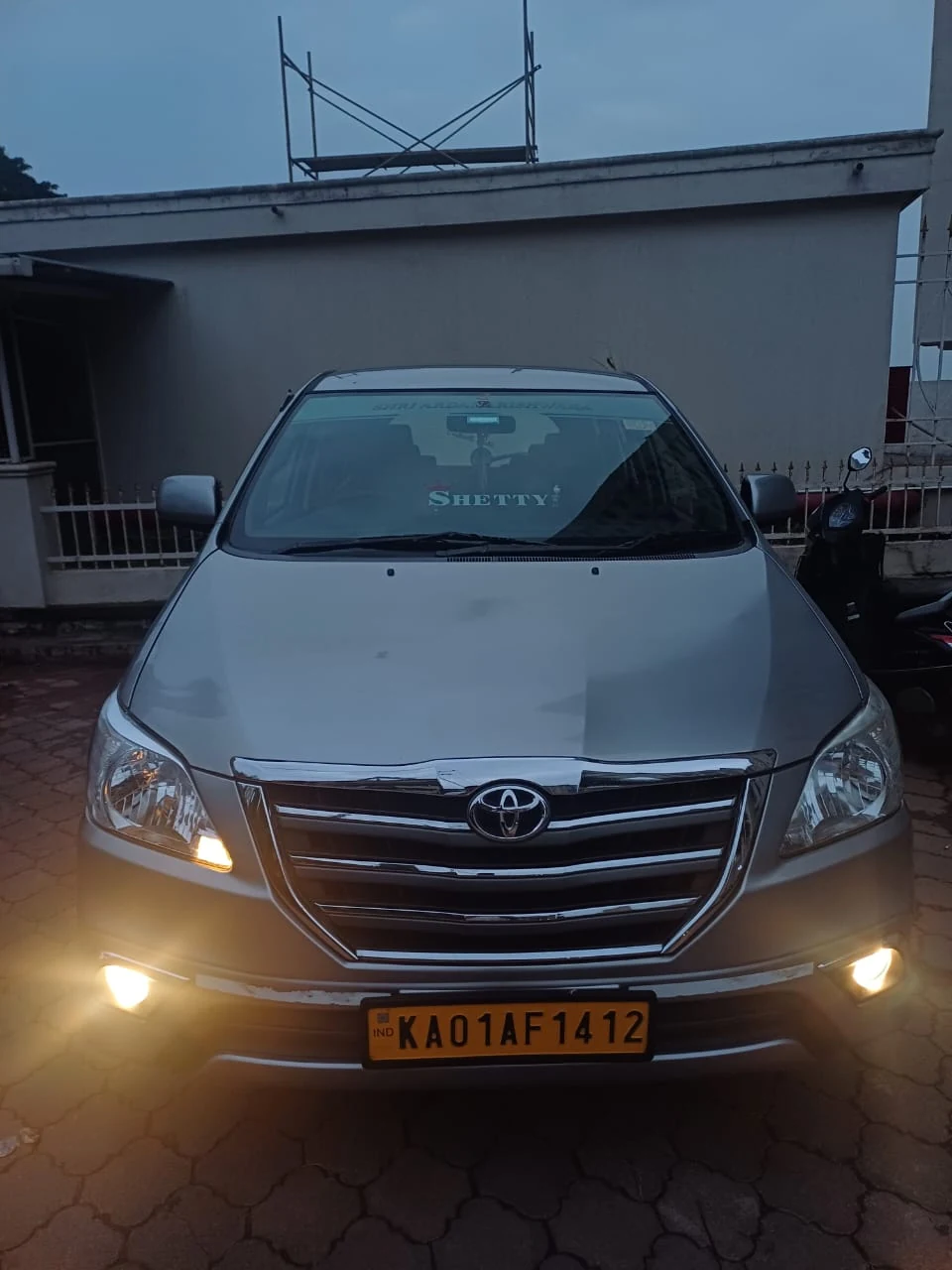 Silver Toyota Innova with Shetty fleet insignia and fog lights illuminated at dusk